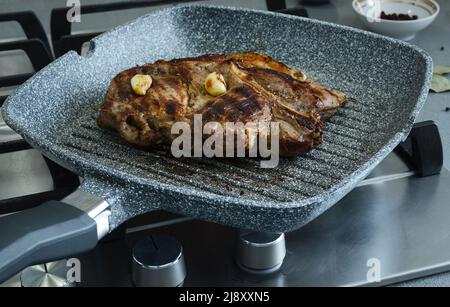Pezzo di carne con aglio, fritto in una padella corrugata. Cottura a base di carne arrosto, bistecche ben fatte Foto Stock