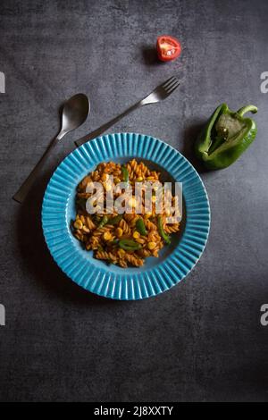 Pasta vegetale a spirale servita in una ciotola blu su sfondo scuro. Vista dall'alto, messa a fuoco selettiva. Foto Stock