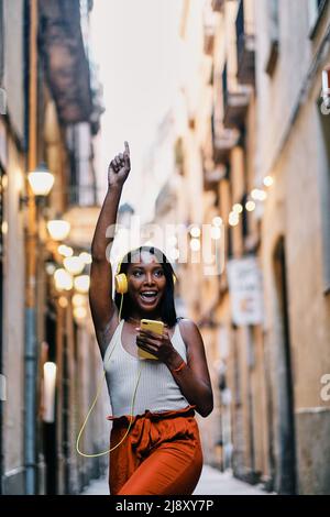Una donna felice che balla mentre ascolti la musica con il telefono cellulare e le cuffie all'aperto. Foto Stock