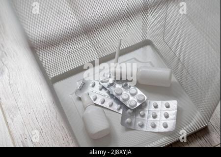 Farmaco in un wastbasket di metallo di maglia bianco. Pillole gettate nel cestino. Un cestino di carta con medicine all'interno su un pavimento di legno. Foto Stock