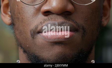 Macro scatto di persona afroamericana muovendo le sue labbra di fronte alla macchina fotografica, avendo pelle naturale sana. Uomo autentico con barba corta e baffi sorridenti, con una rifinitura pulita. Primo piano. Foto Stock