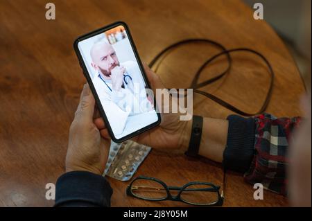 Medicina online. Una donna anziana con sintomi di coronavirus sta parlando su uno smartphone con un virologo. Il medico maschile ascolta le lamentele sul Foto Stock