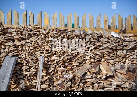 Legna da ardere è accatastata in un cumulo di legno lungo la recinzione contro il cielo blu. Raccogliere legna da ardere per il bagno e riscaldare la casa Foto Stock