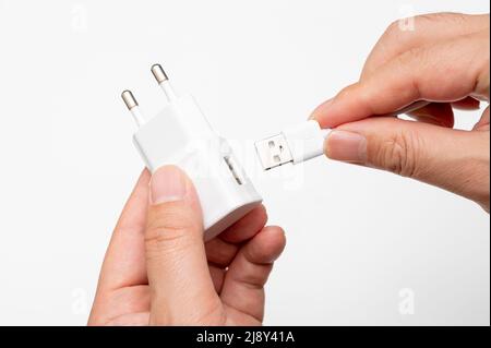 Mano maschio che collega il cavo USB all'adattatore di ricarica. Foto Stock