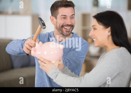 giovane coppia rompendo la banca piggy con il martello a casa Foto Stock