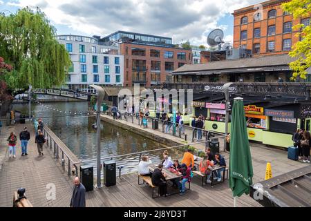 La gente si siede per mangiare all'aperto, in mezzo alla pletora di venditori di cibo al famoso West Yard a Camden Market, Londra, Regno Unito. Foto Stock