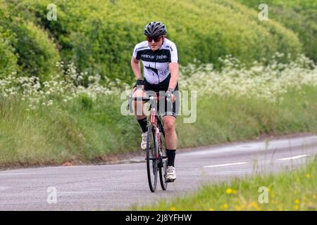 Ciclista vestita in Lycra su una strada di campagna Foto Stock