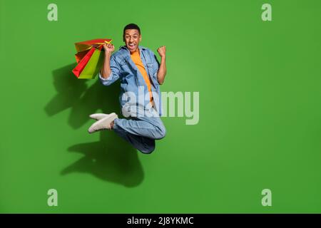 Foto a tutta lunghezza di uomo divertente addicted a shopping saltando in su nell'eccitamento isolato su sfondo verde di colore Foto Stock
