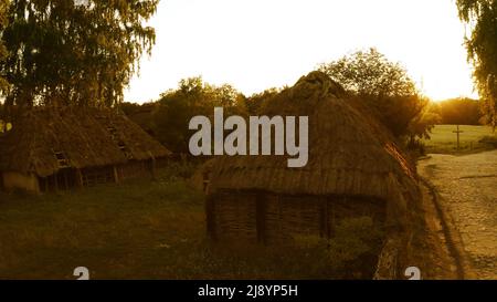 Due antiche capanne in una giornata di sole. Tetto di paglia di capanne. Diversi alberi vicino capanne. Foto Stock