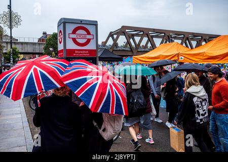 Brick Lane Sunday Market nella zona East End di Londra di Shoreditch in una giornata piovosa. Gli amanti dello shopping e i turisti camminano lungo Brick Lane con gli ombrelloni Union Jack. Foto Stock