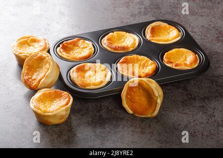 Queijadas o Queijadinhas, piccole cheesecake portoghesi fatte con il primo piano di Queijo fresco in una teglia da forno sul tavolo. Orizzontale Foto Stock