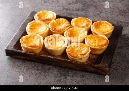 Le saporite mini torte portoghesi Queijadas sono un dolce, cremoso, tradizionale dessert primo piano su un vassoio di legno sul tavolo. Orizzontale Foto Stock