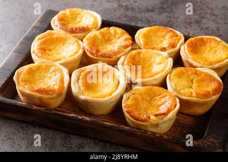 Le torte portoghesi di formaggio Queijadas sono un dolce, cremoso, tradizionale dessert primo piano su un vassoio di legno sul tavolo. Orizzontale Foto Stock