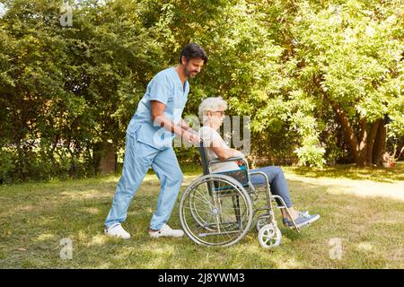 L'infermiera spinge la donna anziana in una sedia a rotelle nel giardino della clinica di riabilitazione dopo un ictus Foto Stock