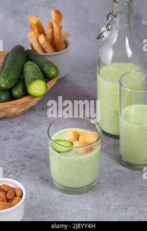 Zuppa di cetrioli refrigerata con noci, erbe aromatiche, yogurt, cracker in un bicchiere di vetro su sfondo grigio. Cibi vegani sani Foto Stock