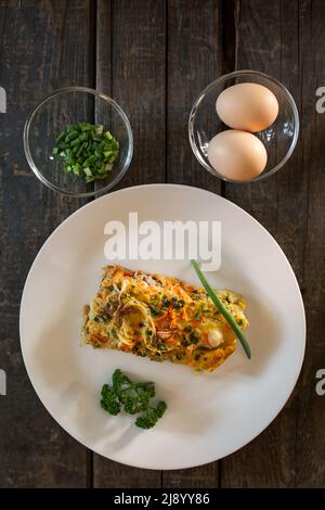 Un pezzo di torta a base di pesce, uova, cipolle e carote. Piatto bianco, tavole di legno Foto Stock