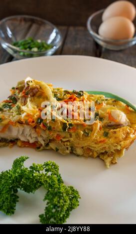 Un pezzo di torta a base di pesce, uova, cipolle e carote. Piatto bianco, tavole di legno Foto Stock