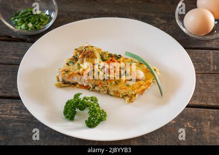 Un pezzo di torta a base di pesce, uova, cipolle e carote. Piatto bianco, tavole di legno Foto Stock