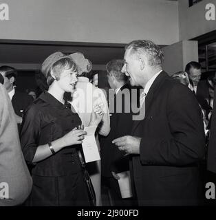 1960s, storica, funzione sociale aziendale, un pranzo formale, ospiti che si riuniscono per le bevande pre-pasto, vediamo un Signore e signora parlare, la donna che tiene un bicchiere di vino in una mano e una sigaretta nell'altra, Inghilterra, Regno Unito. Foto Stock