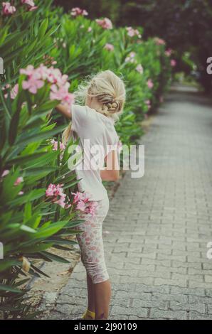 piccola ragazza bionda in navata di fiore di oleandro rosa Foto Stock