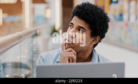 Pensivo maschio africano americano ragazzo sfregamento mento pensare soluzione problema piano strategia di avvio idea seduta con computer portatile maschio scrittore composizione n Foto Stock