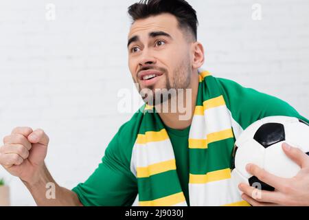 appassionato di sport che tiene il pallone da calcio e pugno di fortuna mentre guarda il campionato Foto Stock