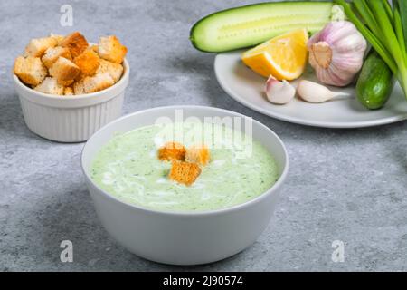 Zuppa fredda di panna vegana con cetriolo, yogurt, aglio, erbe aromatiche, limone e crostini. Concetto di alimento di dieta. Cibo vegetariano e vegano Foto Stock