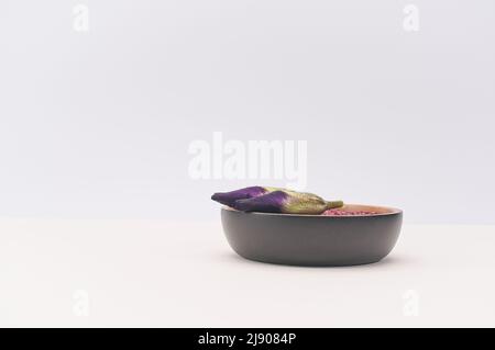 teste di fiori viola iris isolate in un vaso decorativo di legno con sabbia rossa su una superficie bianca del tavolo Foto Stock