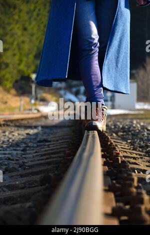 una persona in abiti blu cammina sui binari del treno Foto Stock