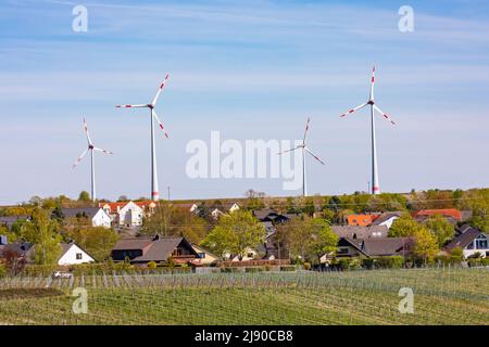 Un insediamento in un paesaggio rurale con campi e vigneti è dominato da enormi turbine eoliche Foto Stock