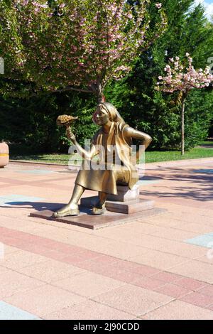 Statua di bronzo di giovane donna che vende fiori con bouqet in mano al parco Foto Stock