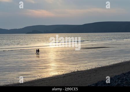 Due persone che camminano sulla spiaggia a Newgale al tramonto, Galles, Regno Unito Foto Stock