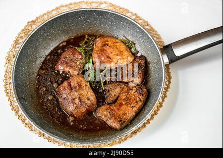 Bistecca di fegato fritta a fette con erbe di rosmarino in padella su sfondo bianco. Foto Stock