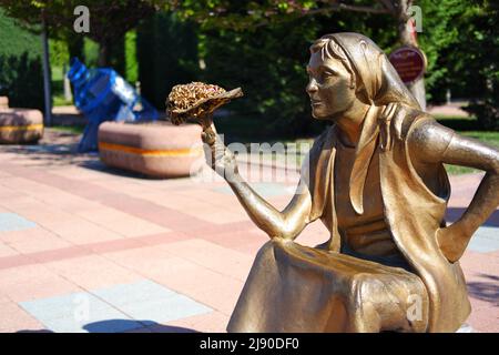 Statua di bronzo di giovane donna che vende fiori con bouqet in mano al parco Foto Stock