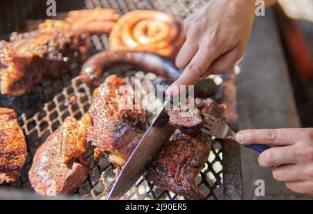 Uomo mani che fanno barbecue per il pranzo. Tagli di carne, serpentine di salsiccia alla griglia e una salsiccia di sangue, manzo su una griglia di ferro. barbecue tradizionale argentino Foto Stock