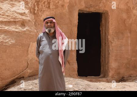 Un uomo arabo locale che indossa il keffiyeh in piedi di fronte ad una porta scolpita nel deserto Rick preteso essere la Grotta di Alibaba Foto Stock