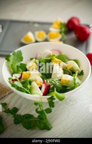 Insalata di primavera fresca con foglie di lattuga fresche, ravanelli, uova bollite in una ciotola su un tavolo di legno Foto Stock