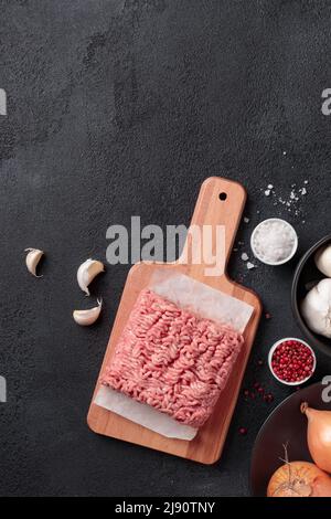 Carne cruda macinata, porzione di carne di farce su un asse di legno su sfondo nero Foto Stock