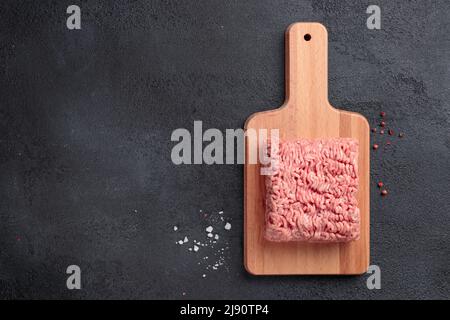 Carne cruda macinata, porzione di carne di farce su un asse di legno su sfondo nero Foto Stock