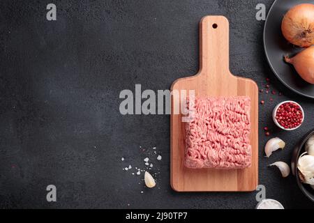 Carne cruda macinata, porzione di carne di farce su un asse di legno su sfondo nero Foto Stock