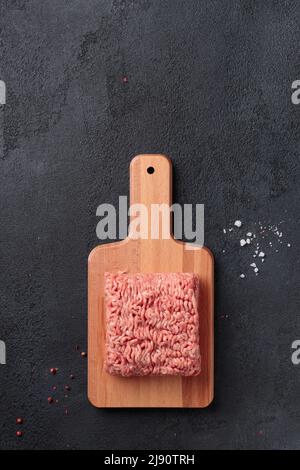 Carne cruda macinata, porzione di carne di farce su un asse di legno su sfondo nero Foto Stock