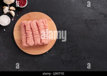 Carne cruda, carne di farsa di pollame su un asse di legno su sfondo nero Foto Stock