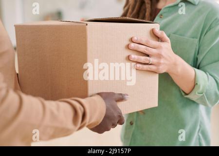 Primo piano di donna irriconoscibile in camicia verde prendendo la consegna di scatola da uomo nero Foto Stock