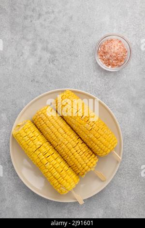 Pannocchie di mais bollite sul piatto e ciotola di sale Himalaya, fondo grigio, piatto Foto Stock
