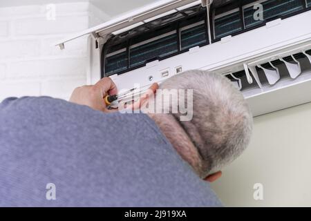 uomo che usa il cacciavite per riparare il condizionatore d'aria all'interno Foto Stock