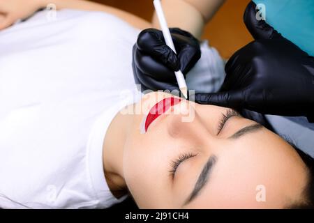 prima della procedura di make-up permanente delle labbra, il maestro cerchia le labbra già fatte con un tratto bianco intorno al contorno Foto Stock