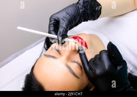 prima della procedura di make-up permanente delle labbra, il maestro cerchia le labbra già fatte con un tratto bianco intorno al contorno Foto Stock