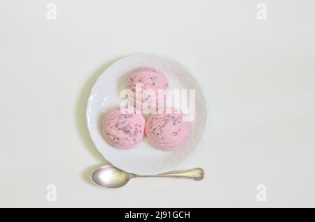 vista dall'alto di tre cucchiai di gelato alla fragola su piatto bianco con cucchiaio, sfondo bianco con spazio per il testo Foto Stock