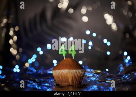 Concetto di biglietto di auguri digitale per le festività o il compleanno. Gustoso cupcake alla vaniglia o muffin con numero 44 quarantaquattro su foglio di alluminio e sfondo chiaro sfocato. Foto di alta qualità Foto Stock