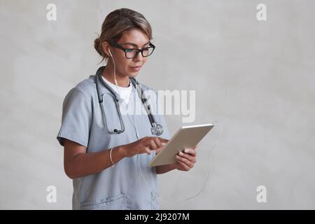 Ritratto orizzontale medio dello studio di bella dottore donna indossando occhiali e cuffie utilizzando tablet digitale Foto Stock